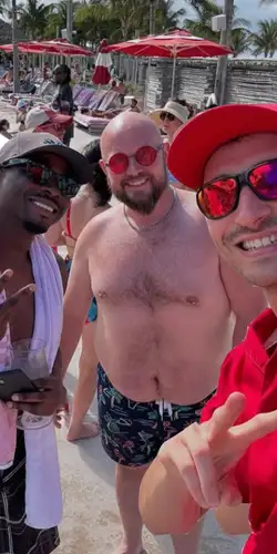 A white gay bear with a black gay chaser, smiling on a beach at Virgin Voyages Bimini Beach Club