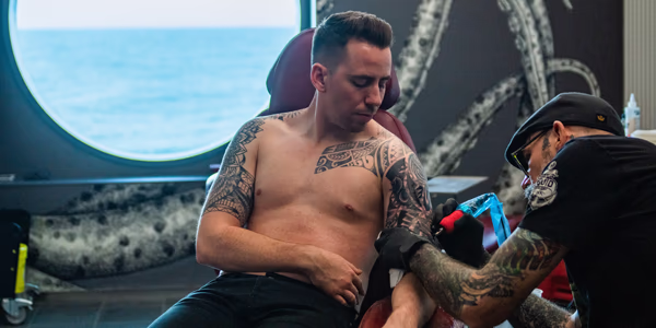 Shirtless guy getting tattoo on Virgin Voyages
